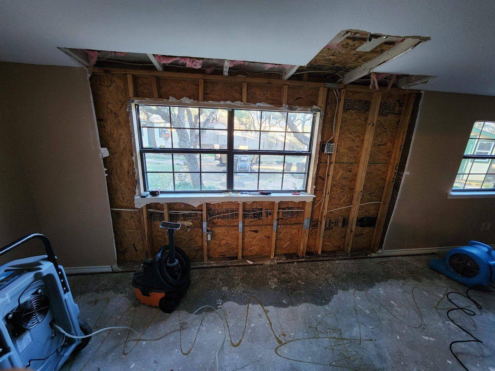 Exterior wall opened at a roof-to-wall junction exposing rotted sheathing and water-damaged framing during storm restoration in Austin
