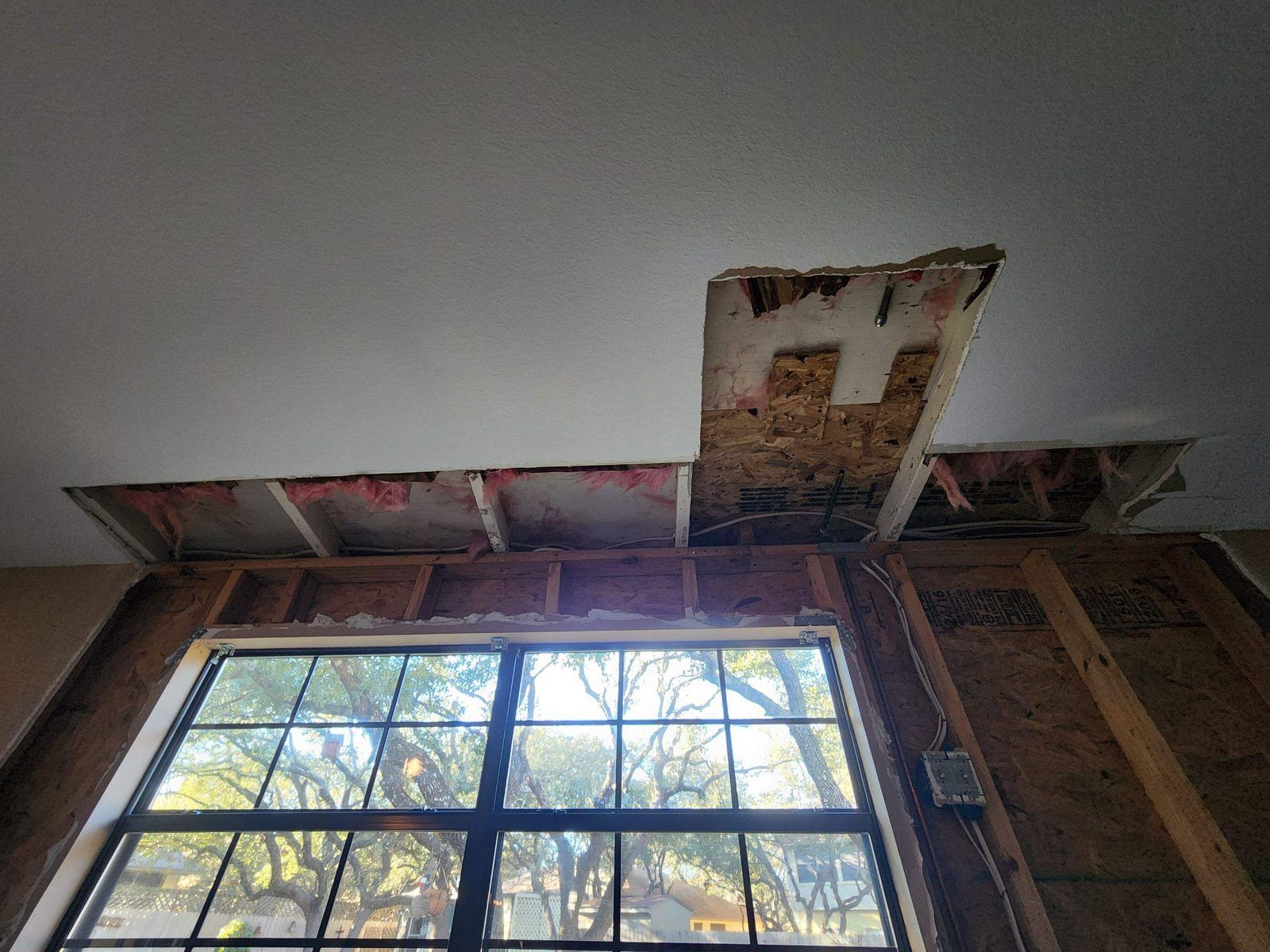 Ceiling drywall removed along an exterior wall to expose wet insulation and roof sheathing after storm-driven water intrusion in an Austin home