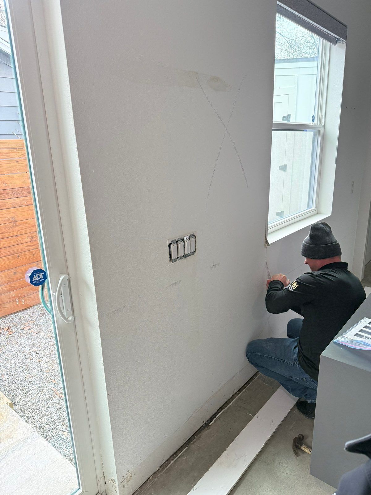 Restoration technician removing baseboard along a wall to open the wall cavity for drying after water damage in an Austin home
