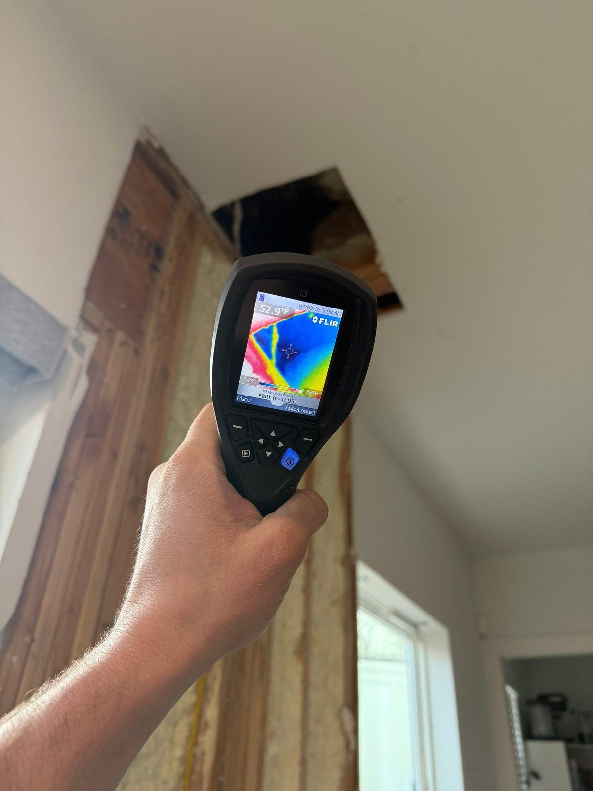 Thermal imaging camera showing a cold blue moisture plume spreading across a ceiling above an opened wall cavity during a water damage inspection in Austin