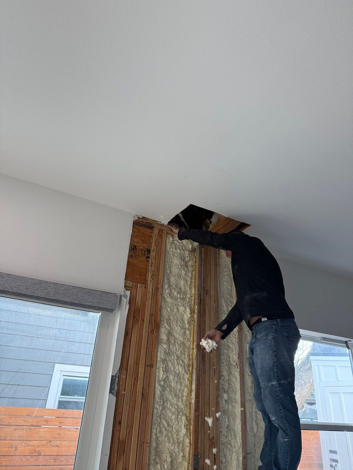 Restoration technician pulling saturated insulation out of an opened ceiling cavity during water damage mitigation in an Austin home